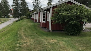 A row of red wooden cabins with white trim, set in a grassy area with trees and a pathway leading to a building in the background. - Finspångs Golfklubbs Stugby (Finspang)