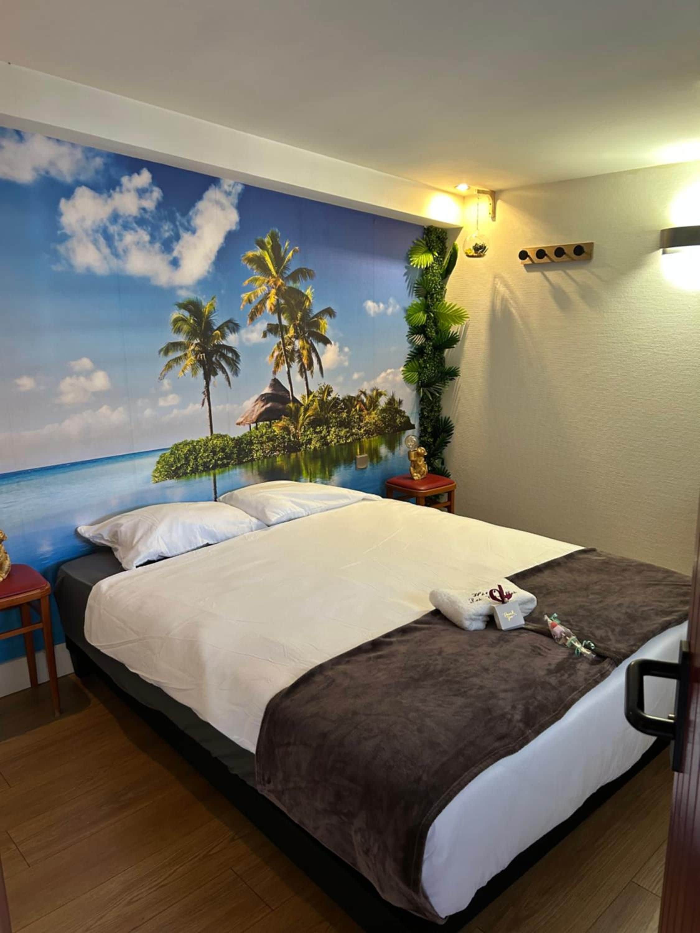 Een hotelkamer met een bed, nachtkastje, wandlamp en een tropisch muurschildering.