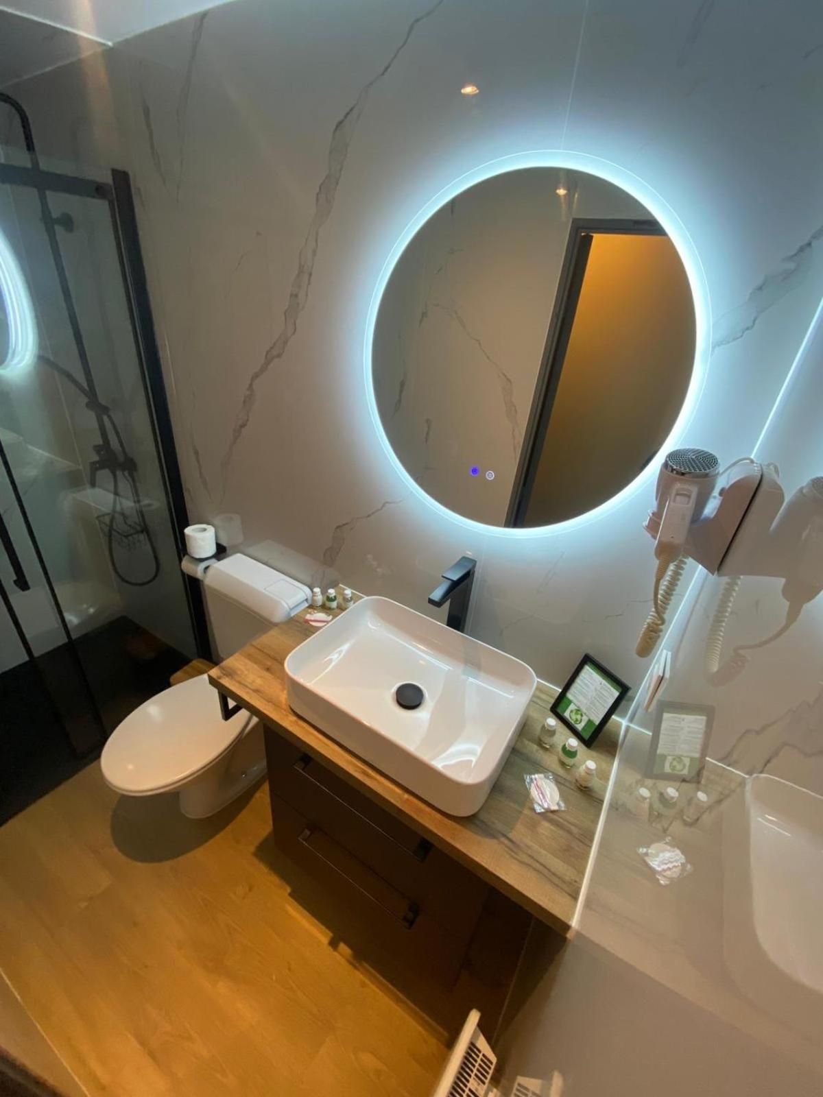 Ein modernes Badezimmer mit Marmorwaschtisch, rundem Spiegel mit Beleuchtung, Toilette und einer Duschkabine aus Glas.