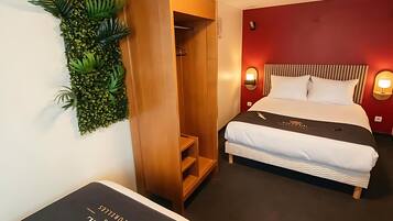 A hotel room with a bed, a wardrobe, a wall-mounted plant, and a bedside table.