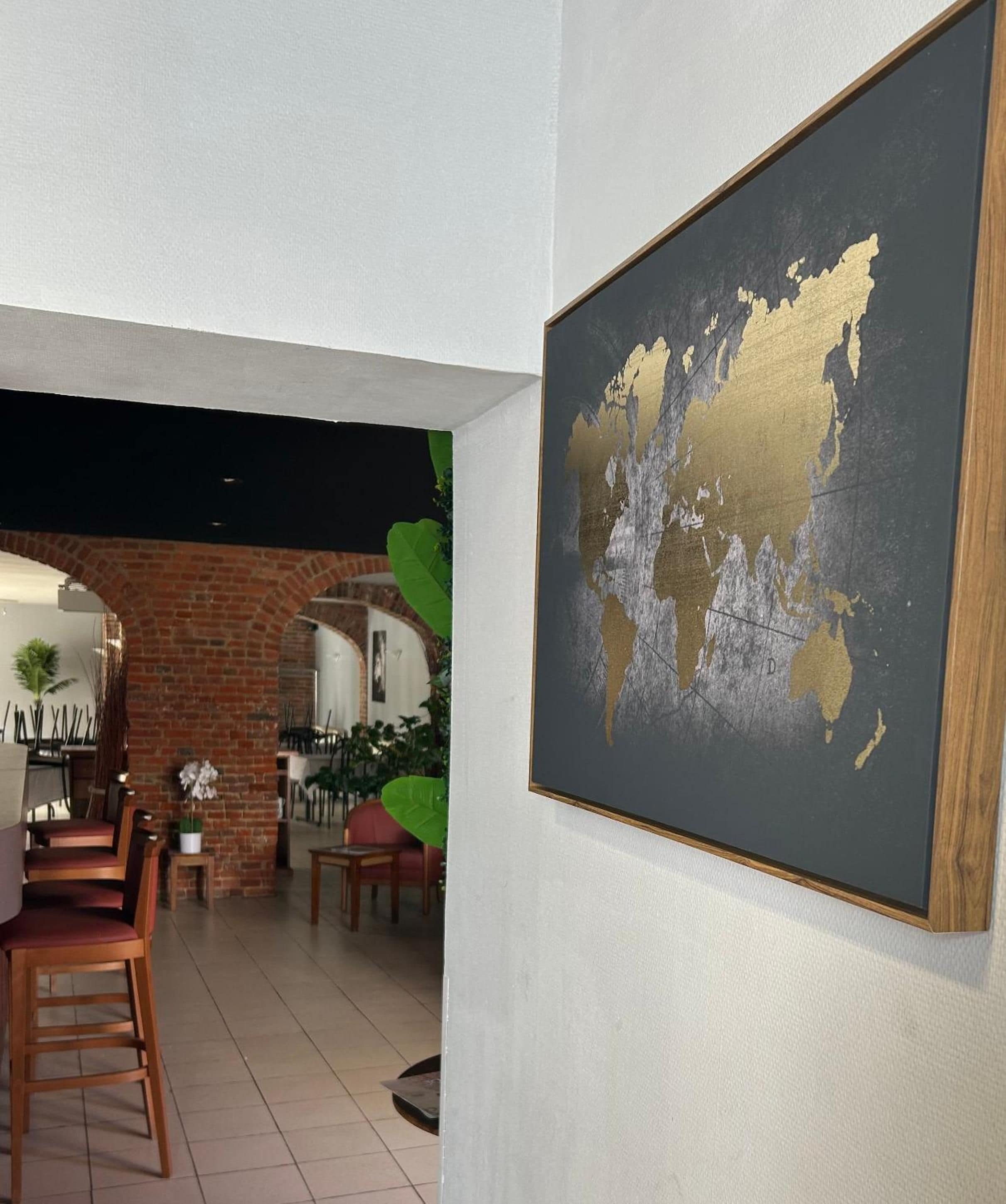 A room with a brick archway leading to a dining area, a large framed world map on the wall, and a plant in the corner.