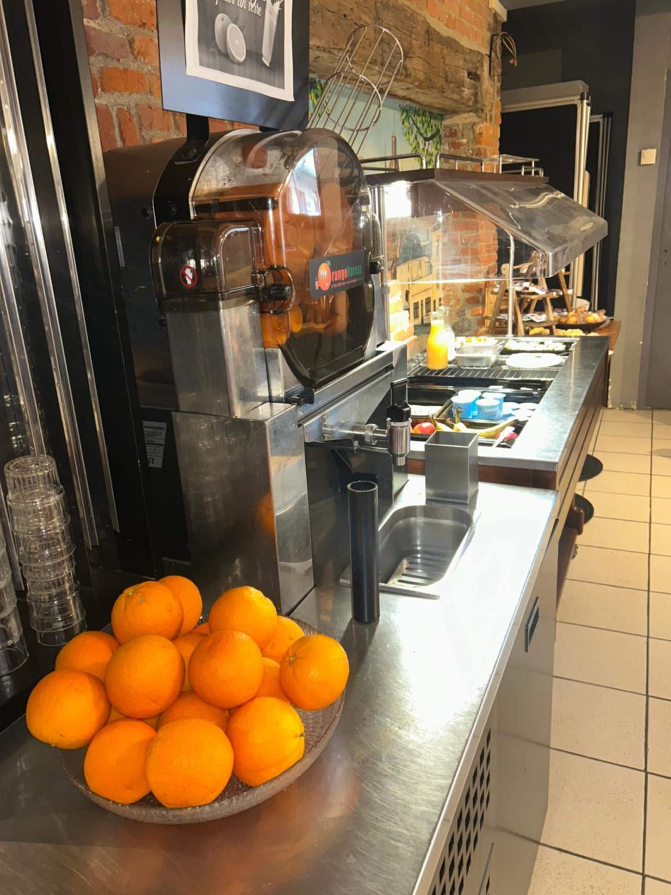 A buffet setup with a coffee machine, a bowl of oranges, and a sink.