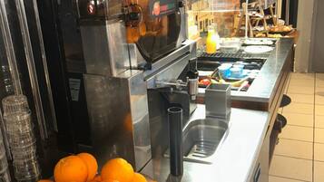A buffet setup with a coffee machine, a bowl of oranges, and a sink.