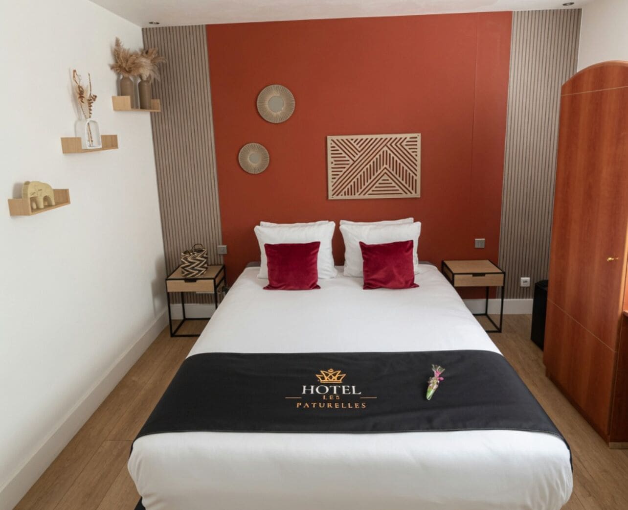 Una habitación de hotel con cama, dos mesitas de noche, un armario y detalles decorativos en la pared.