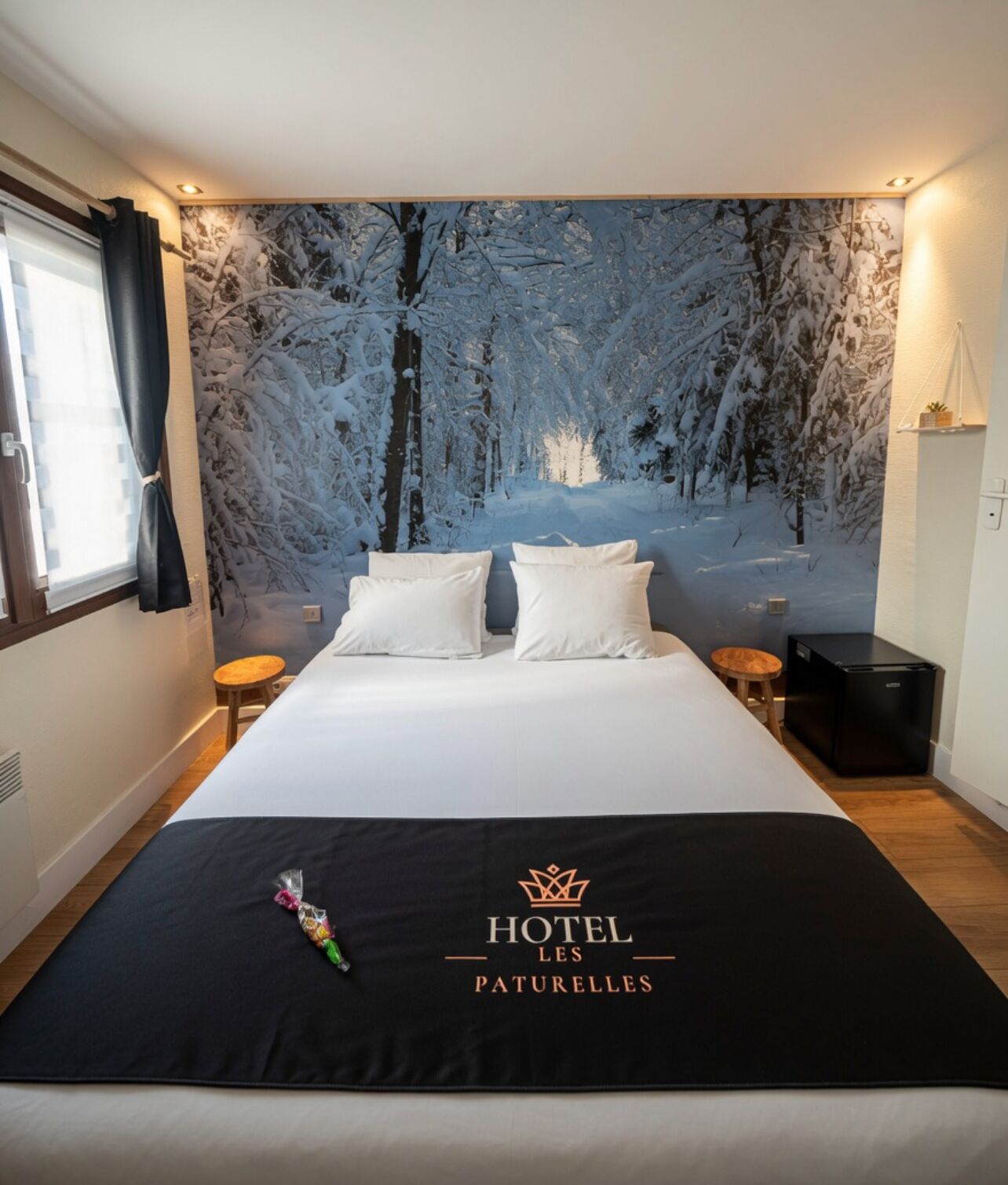 A hotel room with a bed, pillows, a nightstand, a small table, and a wall mural.