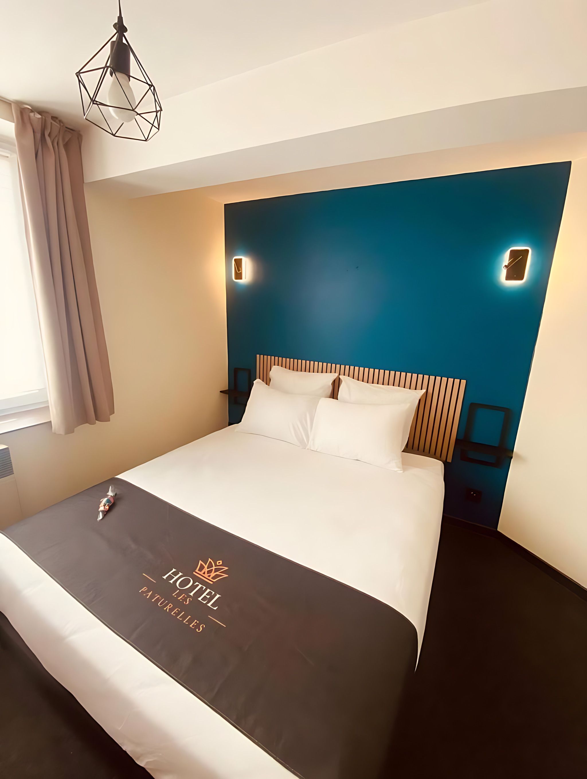 Ein Hotelzimmer mit einem Bett, einem Nachttisch, einer Wanduhr und einer geometrischen Pendelleuchte.