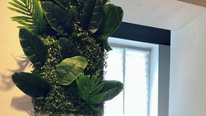 A room with a large indoor plant, a tiger statue, and a window with blinds. - Hôtel Les Paturelles  (Avesnelles)