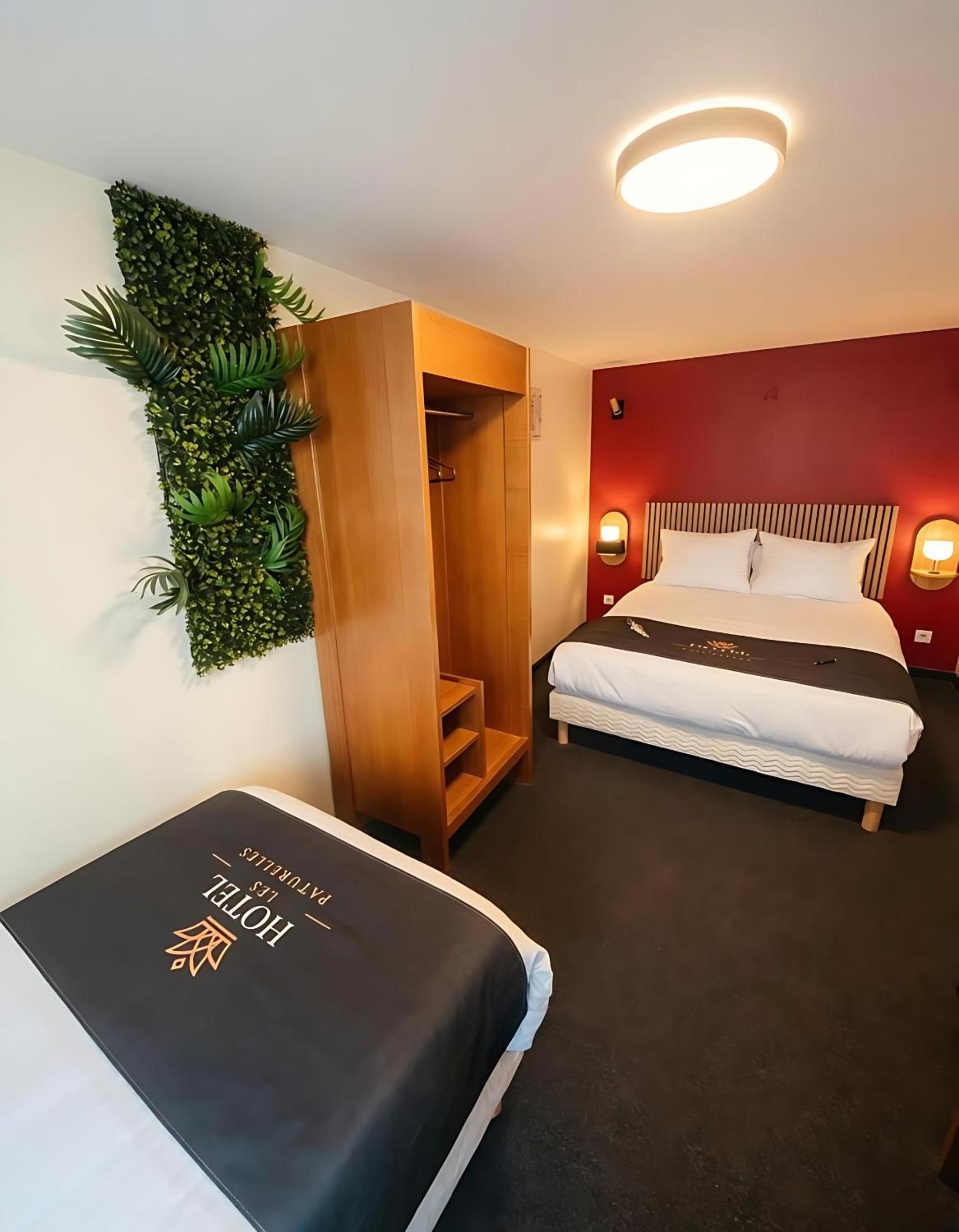 Hotellihuone, jossa on sänky, puinen vaatekaappi, seinälle kiinnitetty kasvi ja yöpöytä.