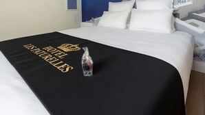 A hotel room with a bed, a black bedspread with text, a white wall, and a large mural of a coastal scene. - Hôtel Les Paturelles  (Avesnelles)