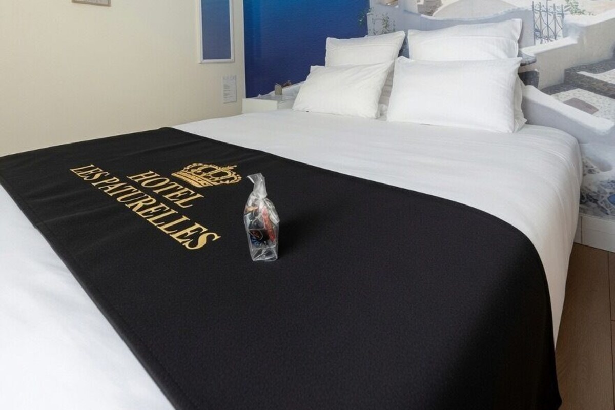 A hotel room with a bed, a black bedspread with text, a white wall, and a large mural of a coastal scene.