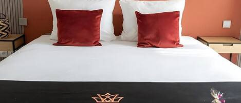 A hotel room with a bed, two pillows, a decorative wall piece, and a sign on the bed.