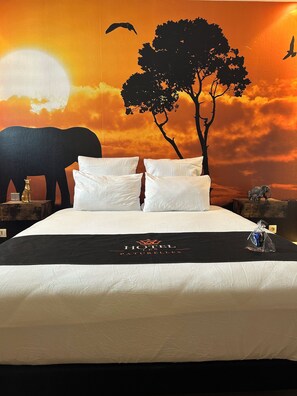 A bed with white linens, a black headboard, and a decorative wall mural depicting a sunset, an elephant, and a tree. - Hôtel Les Paturelles  (Avesnelles)