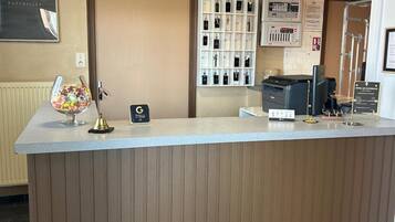 A hotel reception area with a wooden reception desk, a framed sign above it, and a wall-mounted display of toiletries.