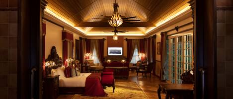 Une chambre d’hôtel spacieuse, dotée d’un grand lit, d’un coin salon avec une table et des chaises, d’un ventilateur de plafond et d’une télévision.