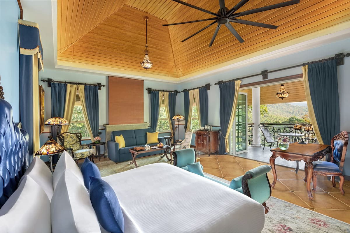 Une chambre spacieuse avec un grand lit, un balcon équipé d’une table et de chaises, et un ventilateur de plafond.