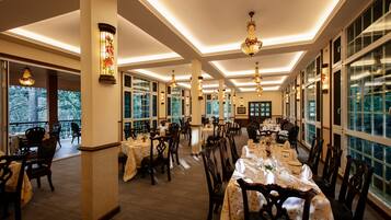 Un comedor amplio con varias mesas dispuestas para comer, ventanas grandes y lámparas decorativas.