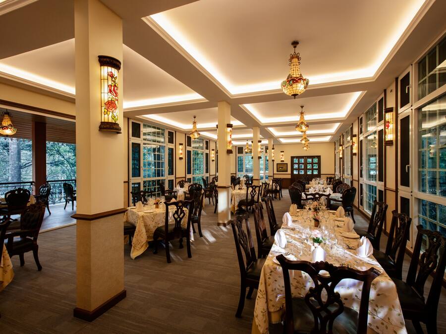 Un comedor amplio con varias mesas dispuestas para comer, ventanas grandes y lámparas decorativas.