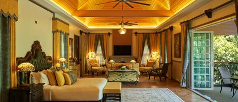 A spacious bedroom with a large bed, a sitting area with chairs, a fireplace, and a balcony with a view.