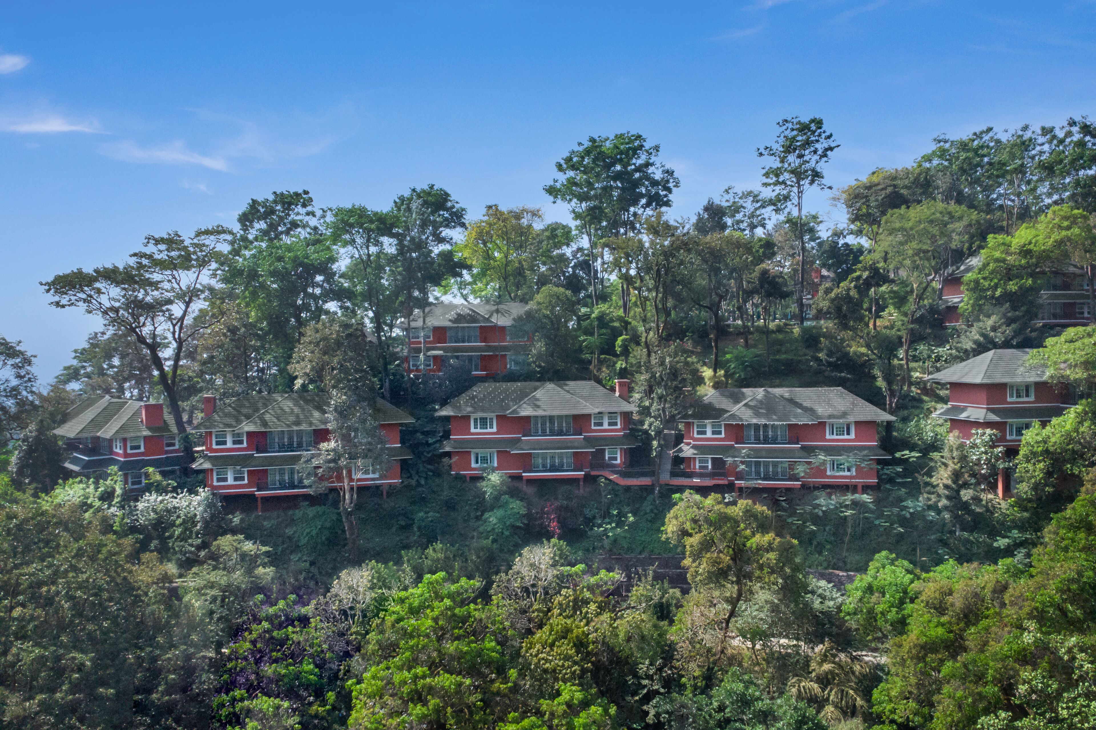 A hillside residential area with multiple red houses, surrounded by dense greenery and trees.