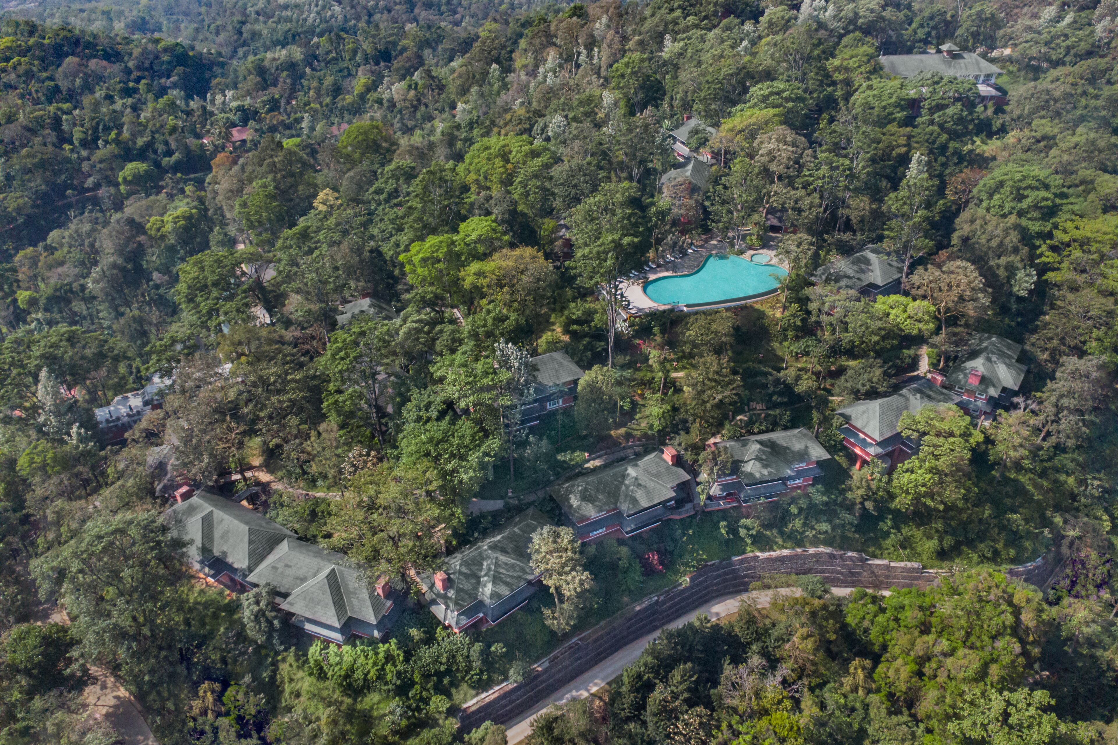 Vista aérea de un complejo turístico con varias construcciones, una piscina y un camino sinuoso.