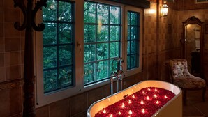 A bathroom with a freestanding bathtub filled with rose petals, large windows, and a wooden ceiling.