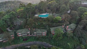 An aerial view of a resort with multiple bungalow-style buildings, a swimming pool, and lush surrounding vegetation.