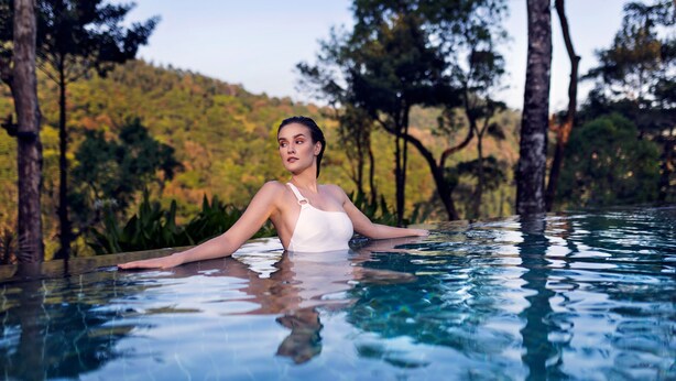 A person in a swimming pool with a natural landscape in the background.