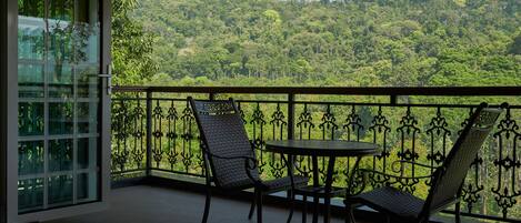 A balcony with two chairs and a small table, overlooking a lush green forested hillside.