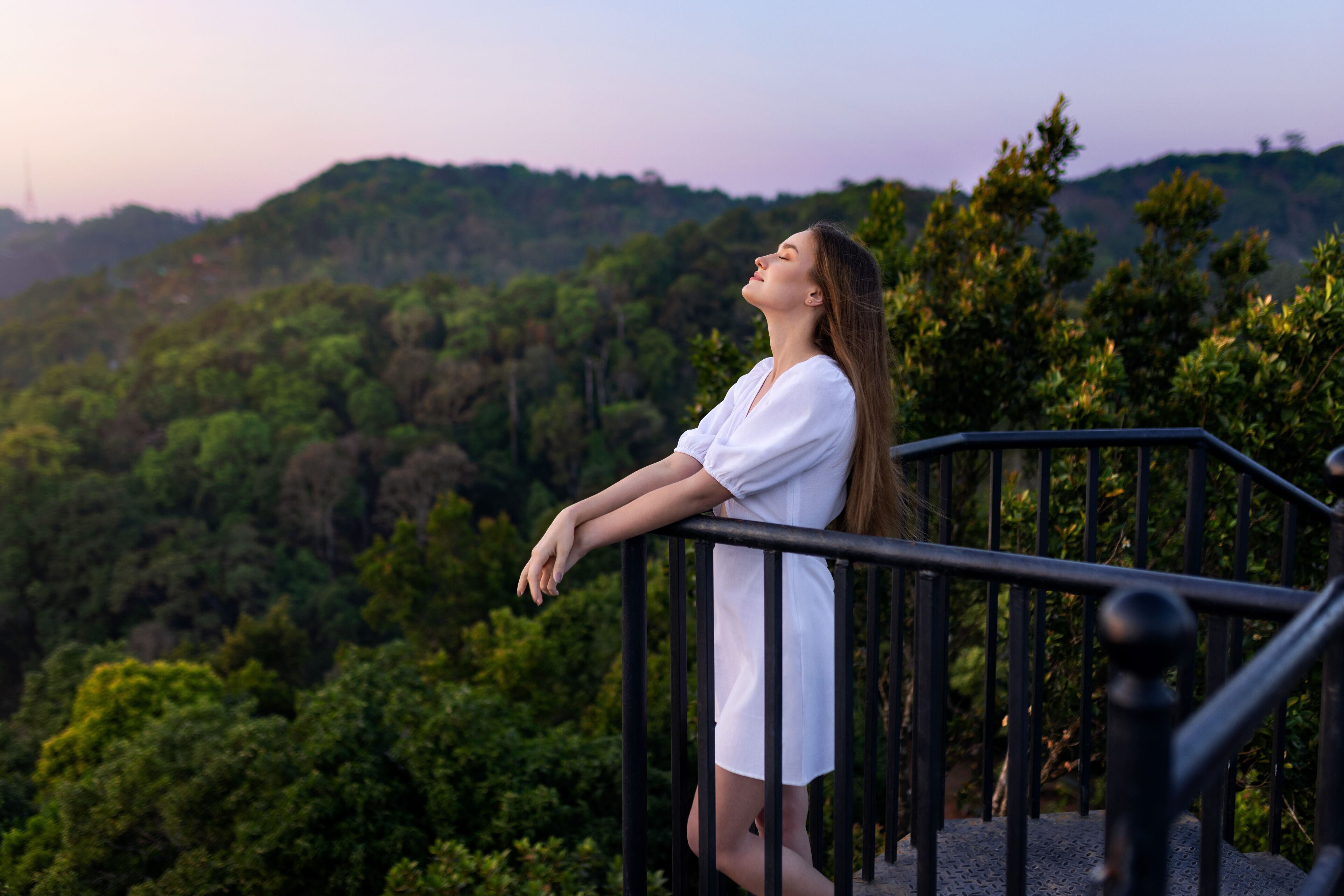 A person standing on a balcony with a view of a forested hillside.