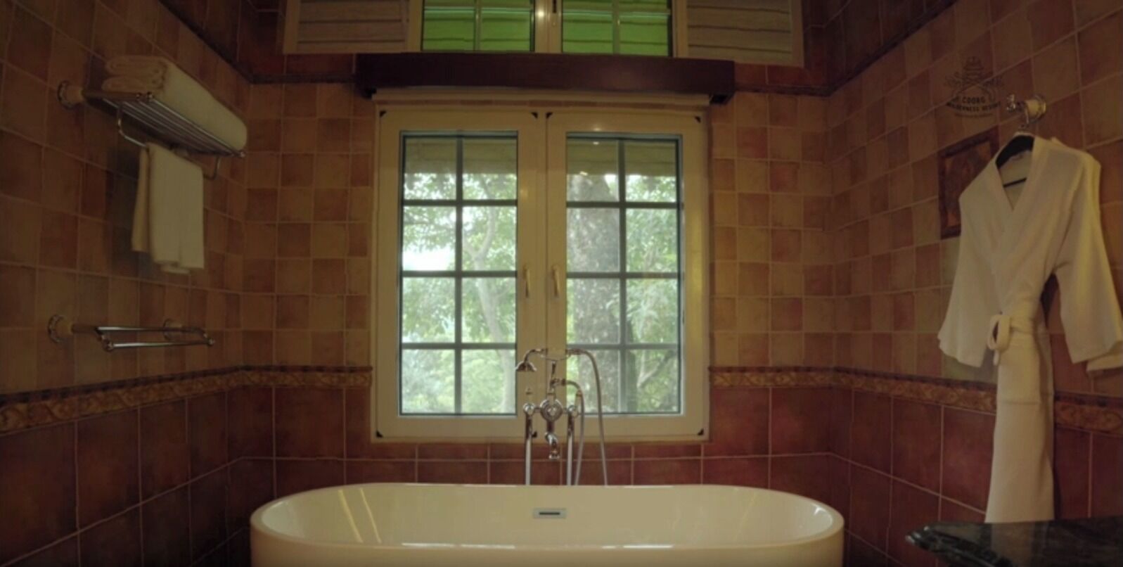 A bathroom with a freestanding bathtub, a window with a view of trees, and a towel rack with a robe.
