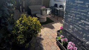 A patio area with a seating arrangement, potted plants, and a stone wall. - Holiday summer style house, family or couple. With privacy/little garden/ sea (Noordwijk aan Zee)