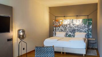 A modern hotel room with a large bed, a flat-screen TV, a floor lamp, and a wall with abstract art.