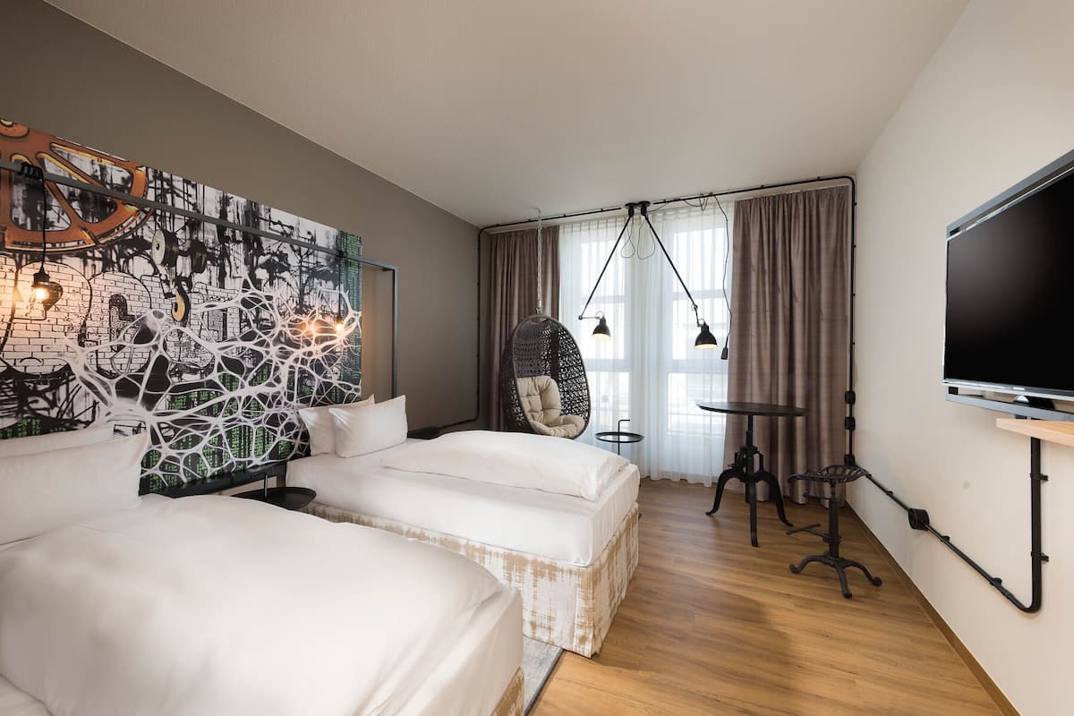 A hotel room with two beds, a large mural on the wall, a television, and a chair.