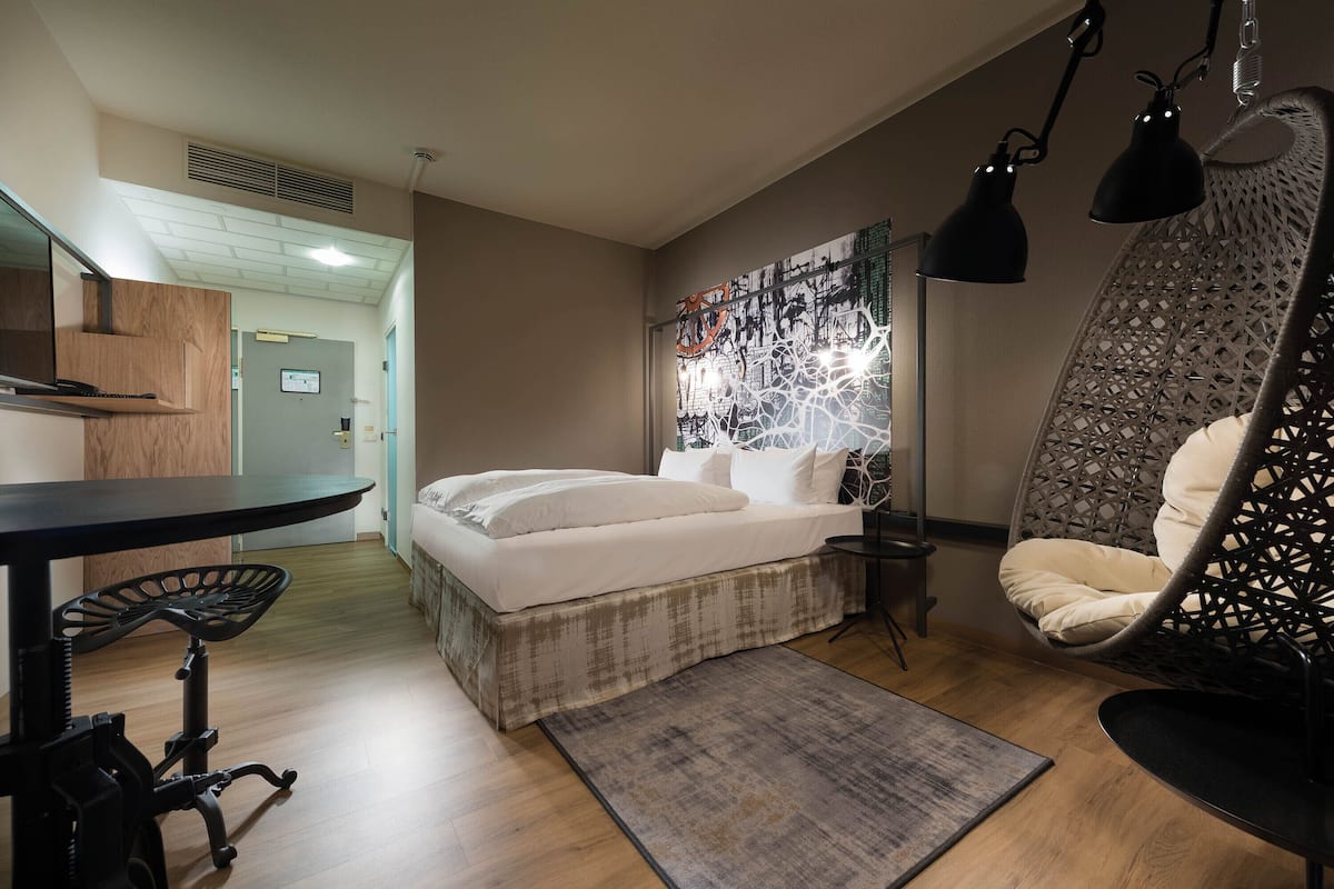 A modern bedroom with a bed, a desk, a chair, and a hanging chair.