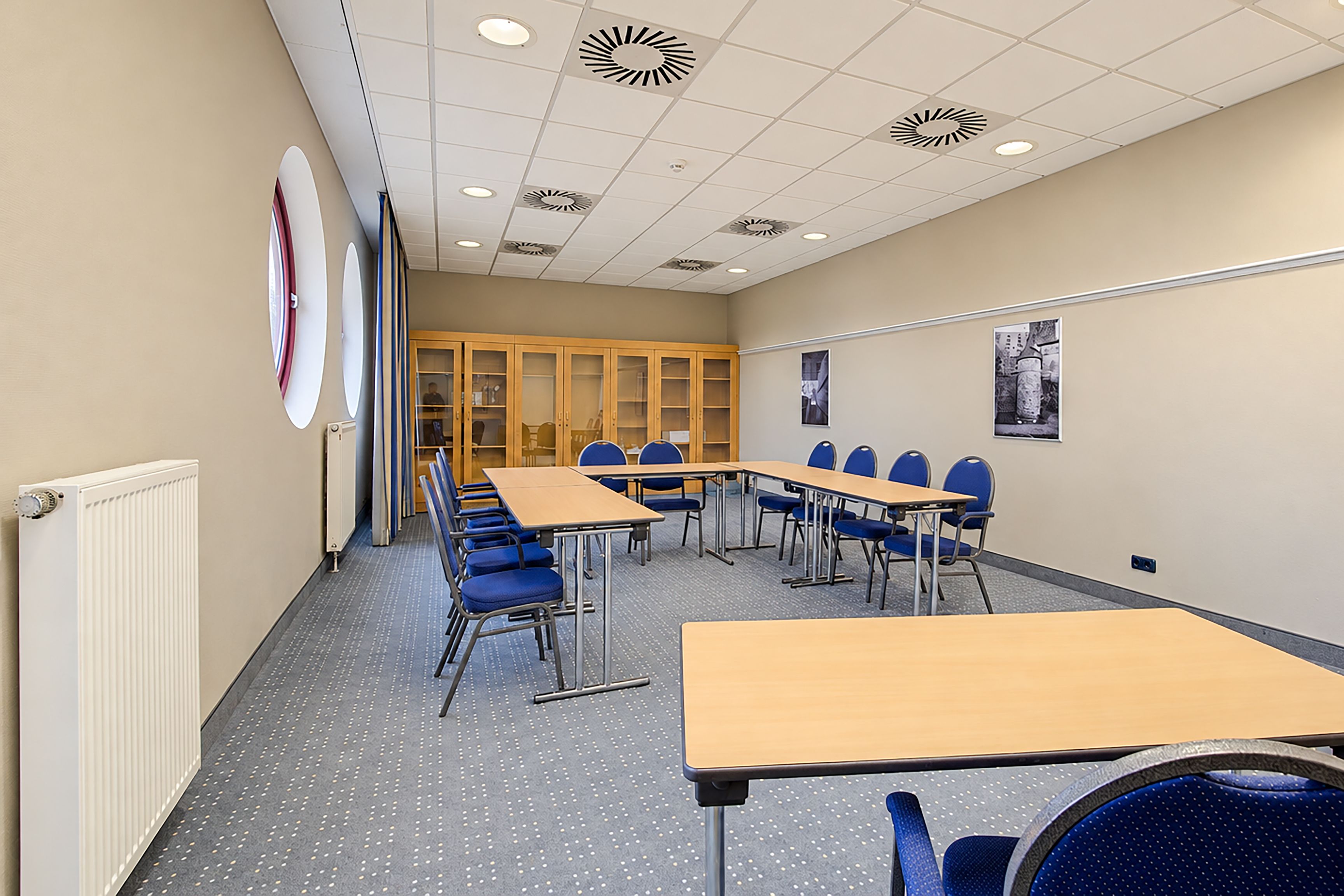 Ein Konferenzraum mit einem langen Tisch, blauen Stühlen und einer weißen Decke mit runden Leuchten.