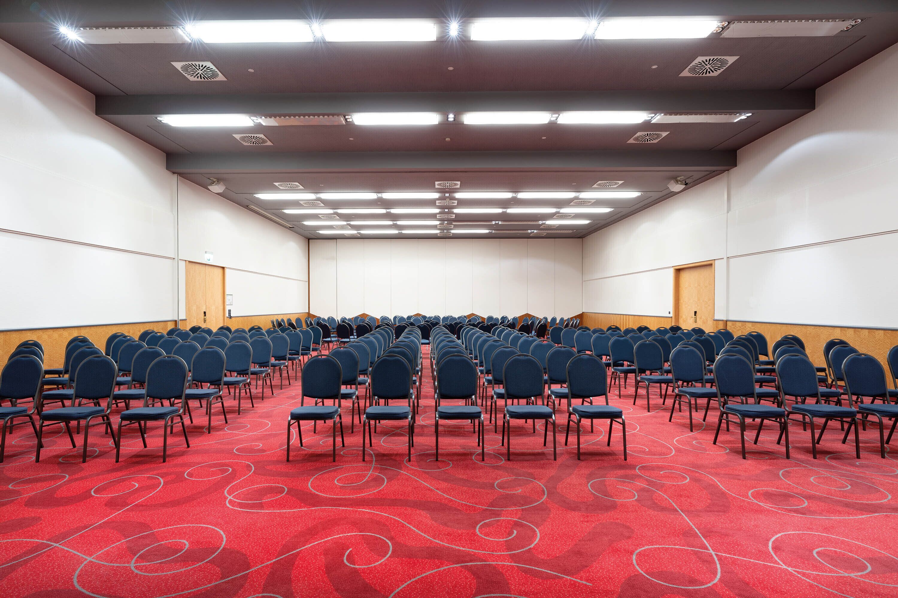 A conference room with rows of chairs, a red carpet, and a whiteboard on the wall.