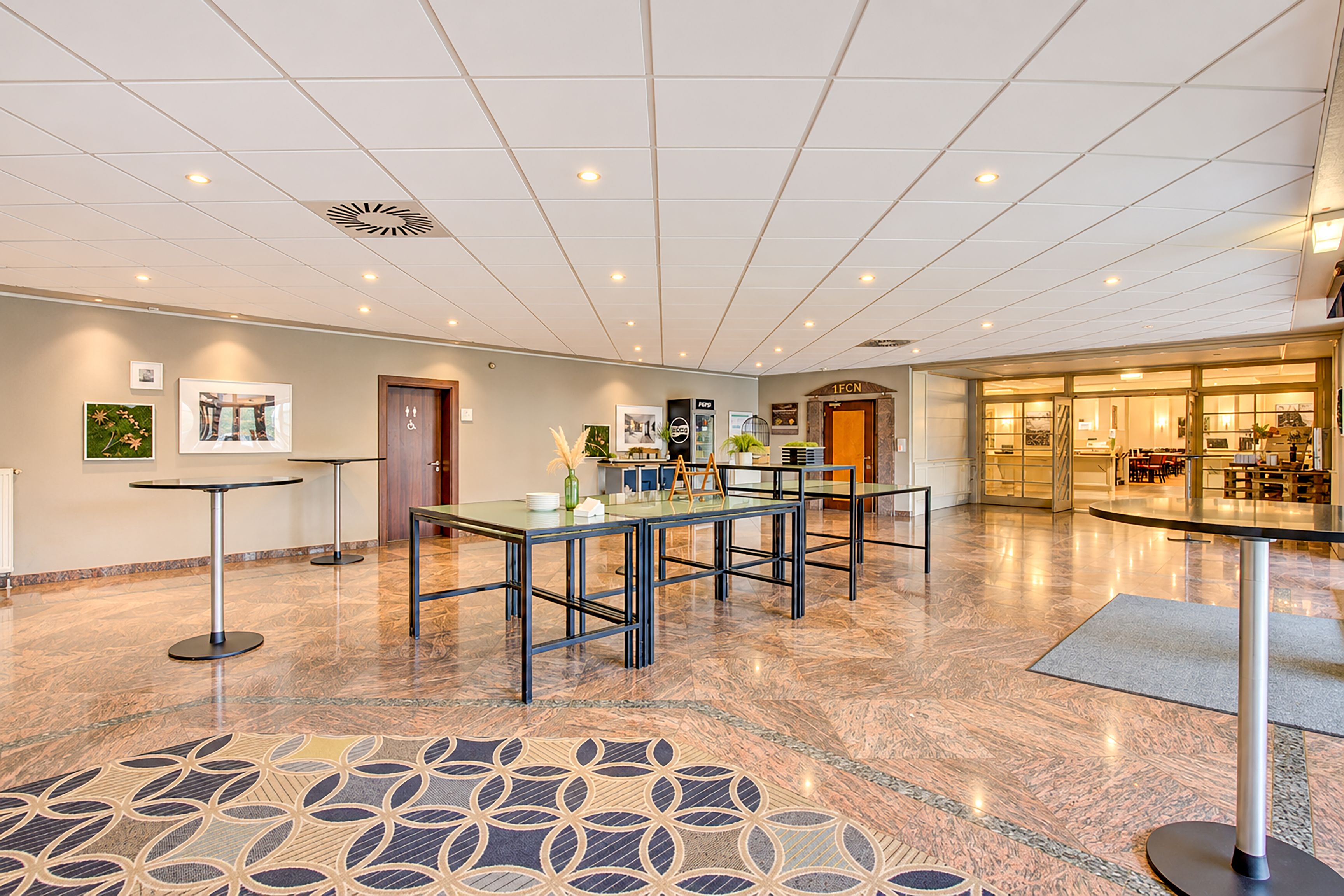 Un'ampia hall con pavimento in marmo, una reception e un divisorio in vetro che separa la hall da una sala ristorazione.