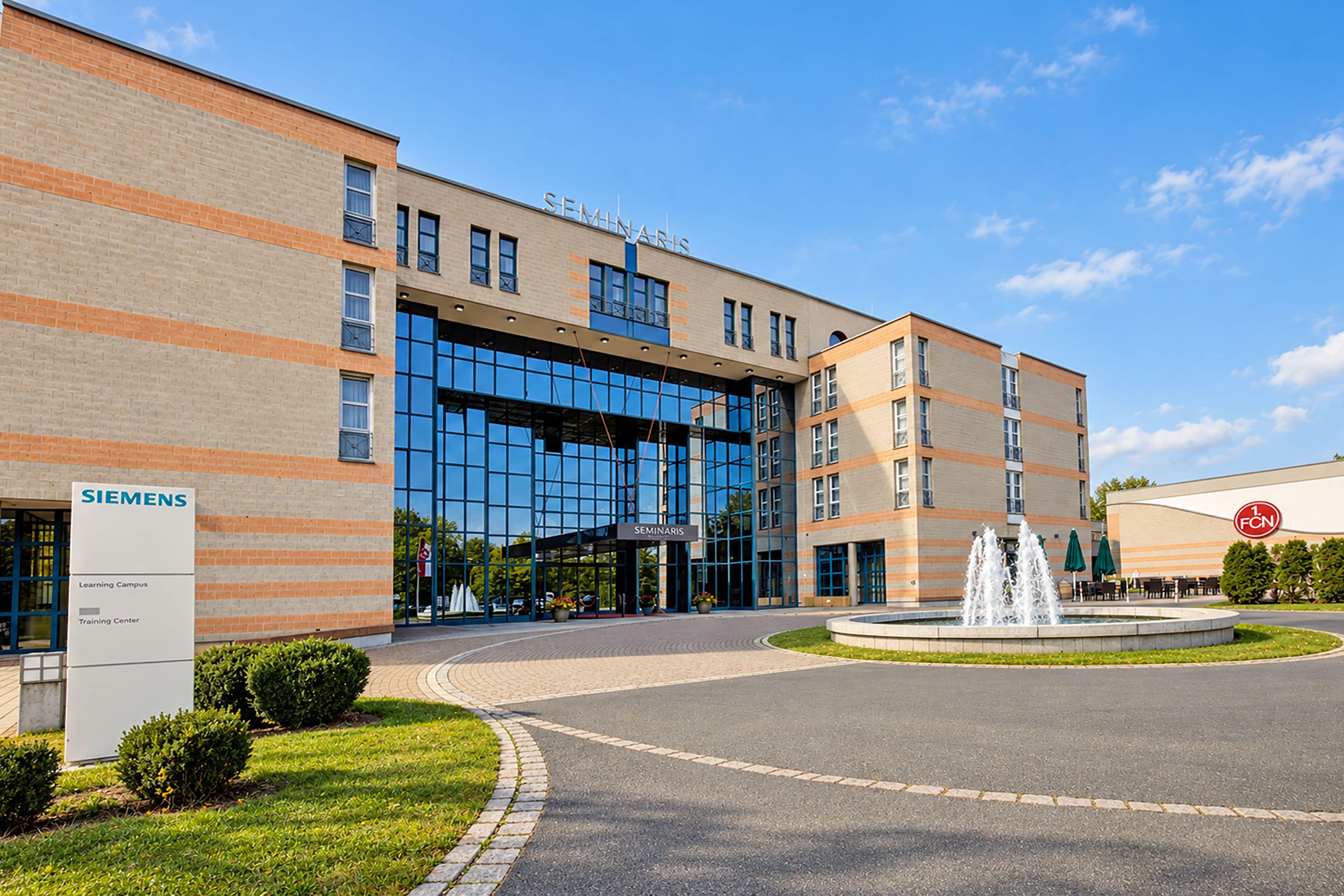 Ein modernes Gebäude mit einer großen Glasfassade, auf dem 'SEMINARIS' steht, und ein Schild des Siemens Learning Campus.