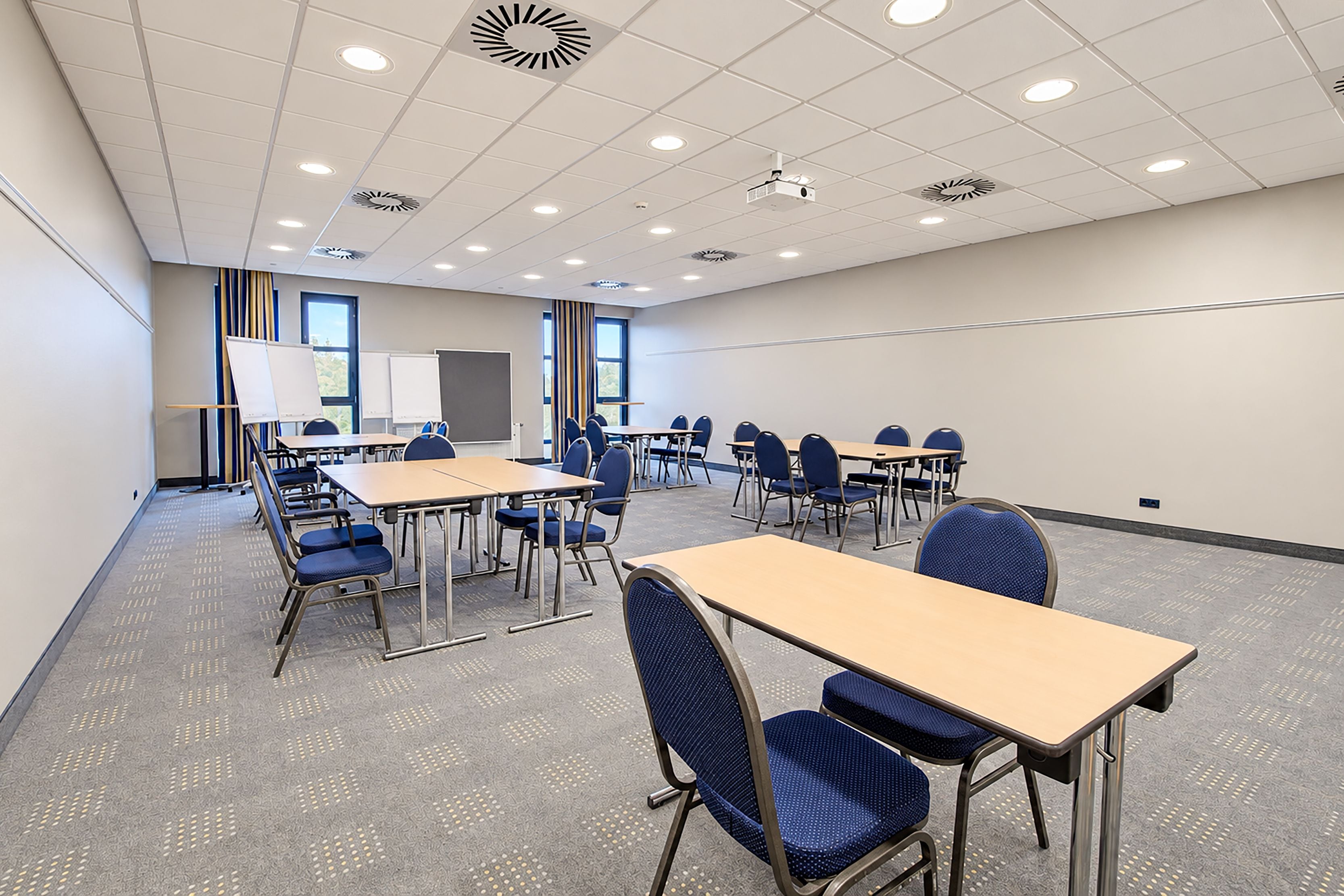 A conference room with multiple tables and chairs, whiteboards, and a projector.