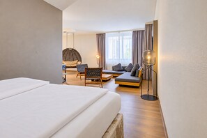 A hotel room with a large bed, a sofa, two chairs, a hanging chair, a floor lamp, and a view of the outdoors through the window.