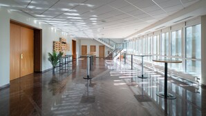 Un vestíbulo amplio con piso pulido, una escalera y una fila de mesas y sillas.