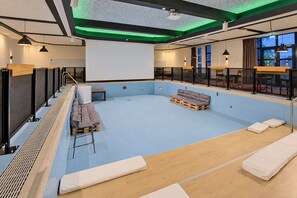 A modern indoor swimming pool with a blue tiled floor, wooden deck, and seating areas.