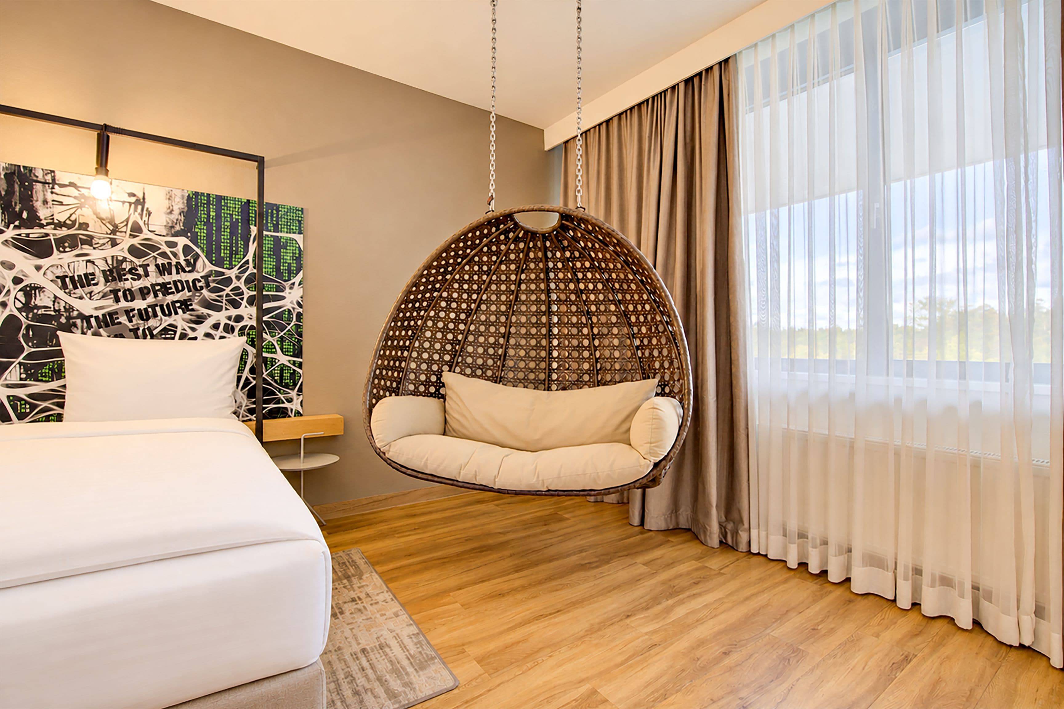 Un dormitorio moderno con una silla colgante, una cama, una obra de arte en la pared y un ventanal con cortinas.