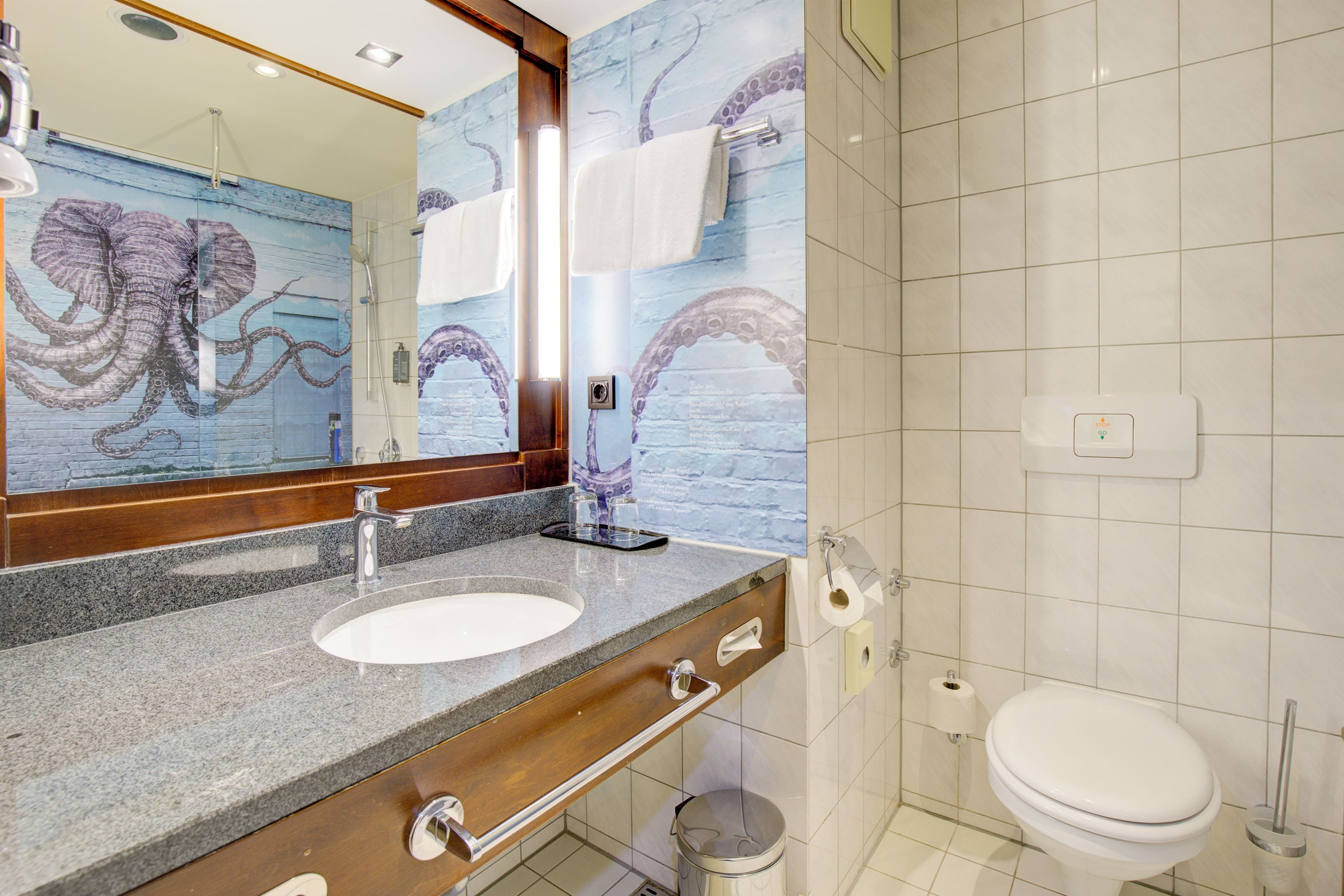 A bathroom with a marble sink, a mirror, a toilet, and a wall with an octopus mural.