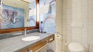 Un baño con lavamanos de mármol, espejo, inodoro y pared con un mural de pulpo.