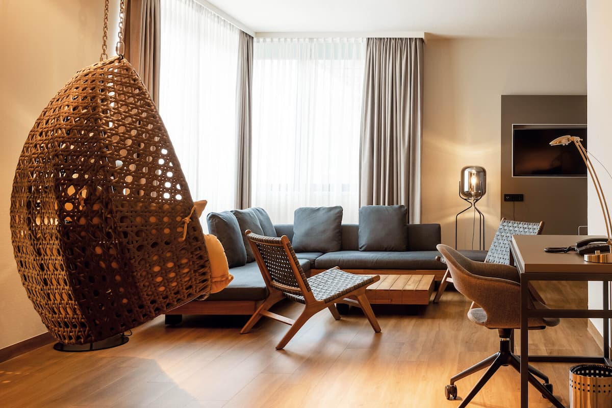 A modern living room with a hanging chair, a sofa, and a desk with a lamp.