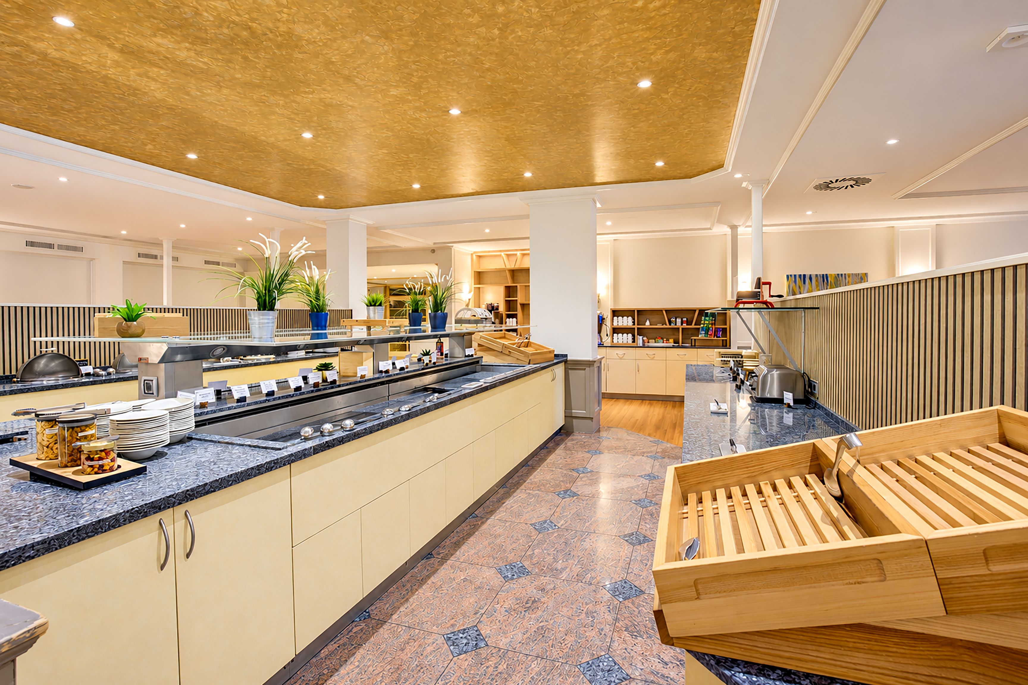Una cocina moderna de hotel con barra libre, asientos de madera y piso de baldosas.