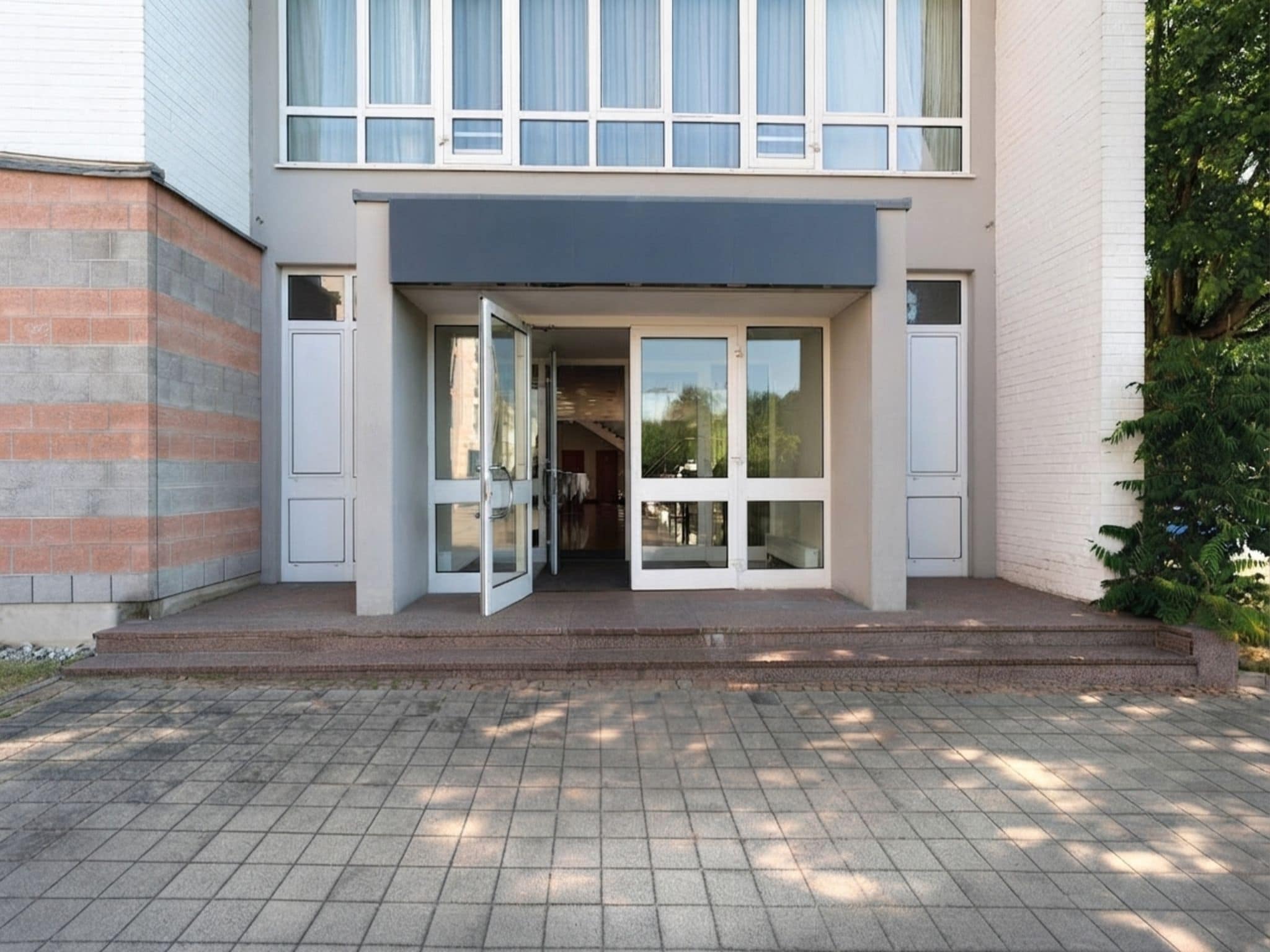 Ein modernes Gebäude mit Glastür, Ziegelverkleidung und einem gepflasterten Eingangsbereich.