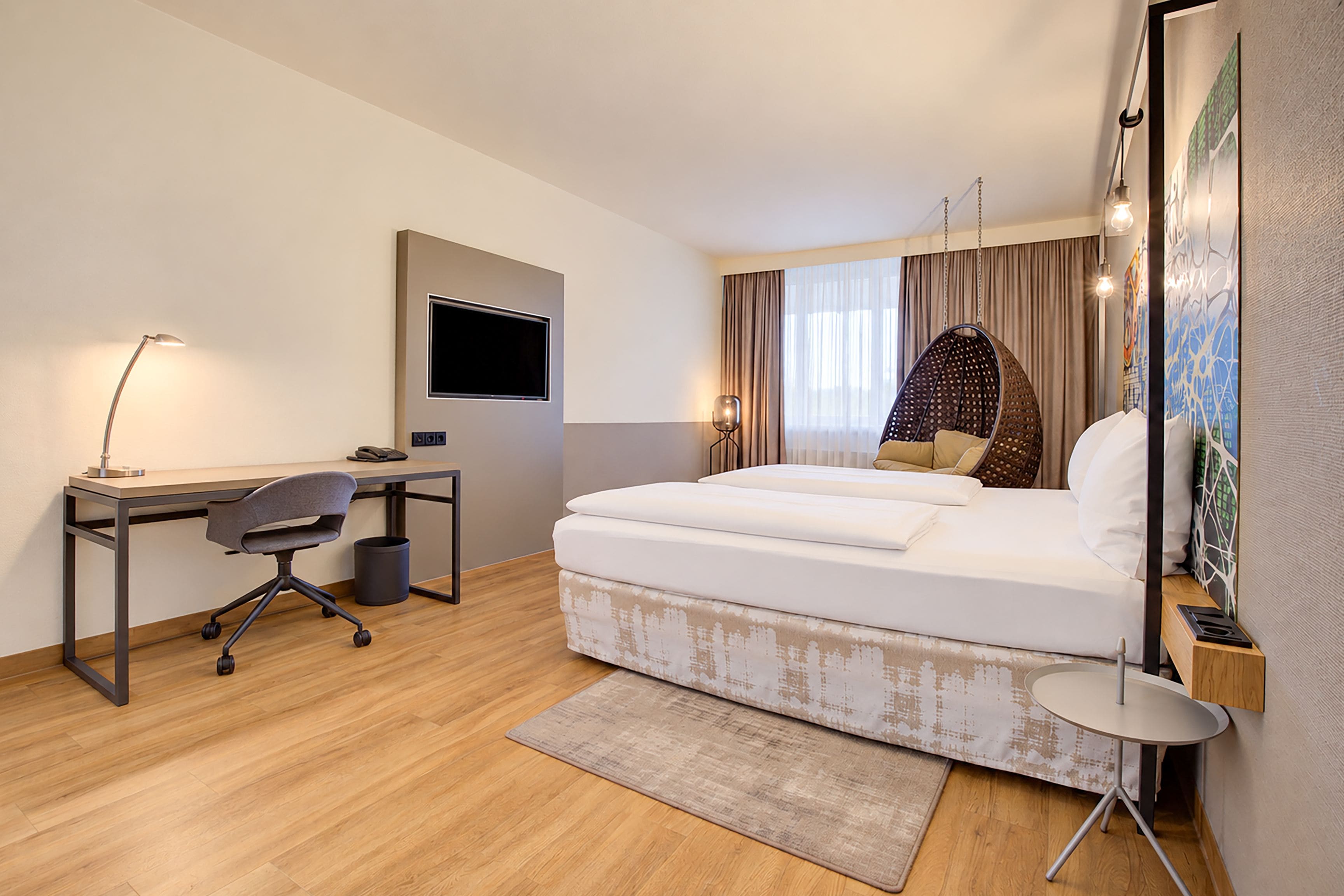 Ein modernes Hotelzimmer mit Bett, Schreibtisch, Stuhl und einem großen Fenster mit Vorhängen.