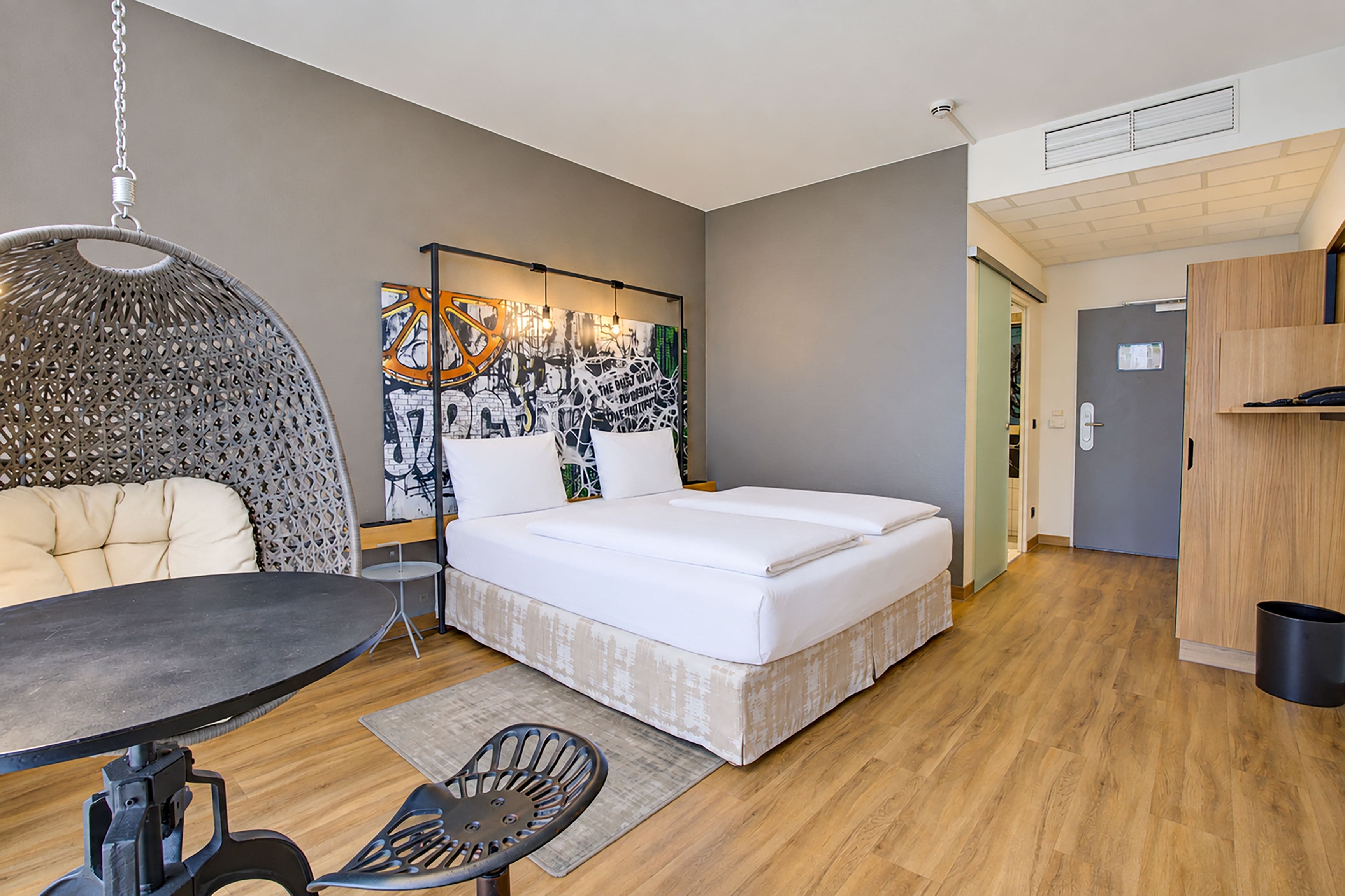 Ein gemütliches Schlafzimmer mit Bett, Pendelleuchte, kleinem Tisch und Stuhl.